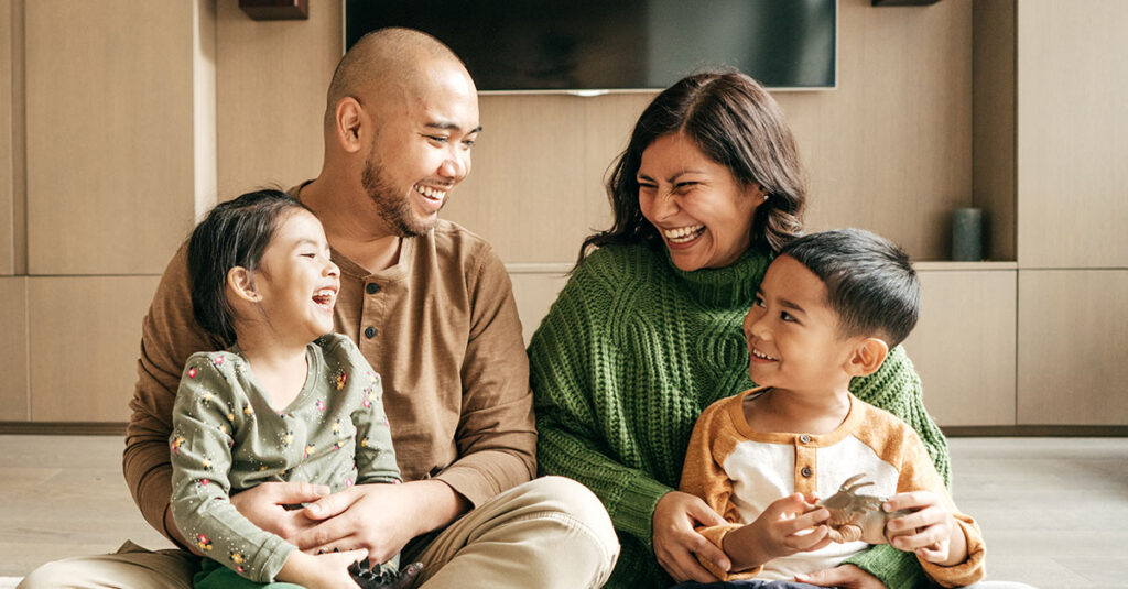 A married Veteran couple laughing with their two children at home.