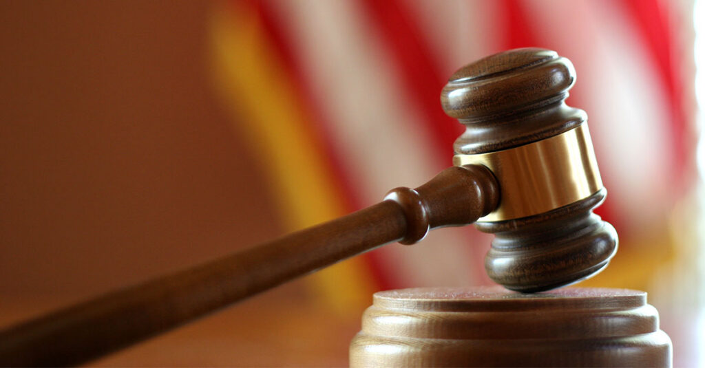 An image of a gavel resting on a gavel pad with the American flag blurred in the background.